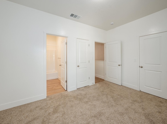 unfurnished bedroom featuring light carpet and ensuite bathroom