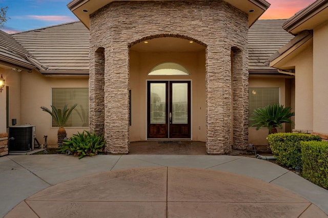 exterior entry at dusk with french doors, cooling unit, and a patio area