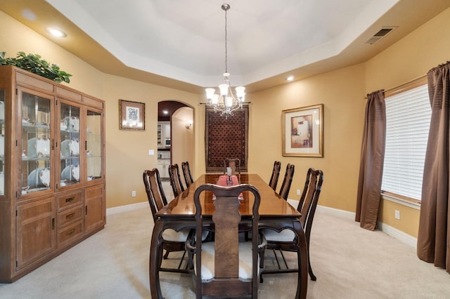 carpeted dining area with an inviting chandelier and a raised ceiling