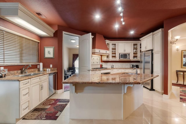 kitchen featuring sink, a large island, light stone countertops, appliances with stainless steel finishes, and premium range hood