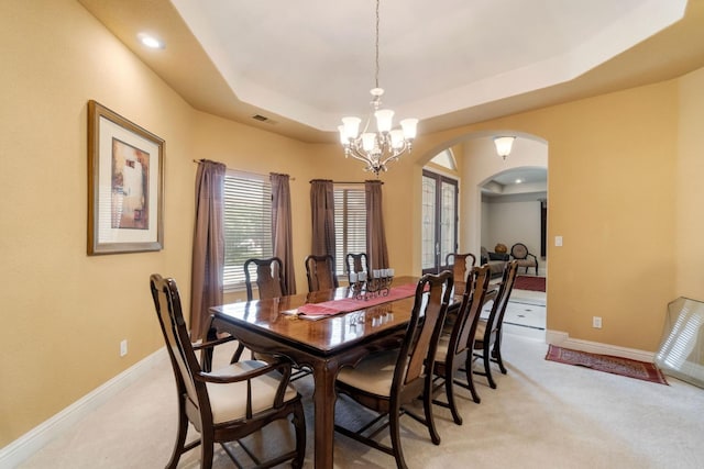 dining room with light colored carpet, a chandelier, and a raised ceiling