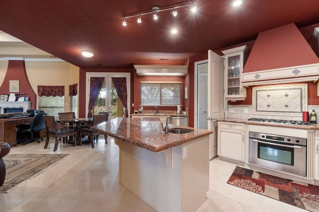 kitchen with stainless steel appliances, white cabinetry, sink, custom range hood, and backsplash