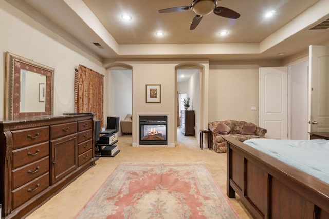 carpeted bedroom with a multi sided fireplace, ceiling fan, and a raised ceiling