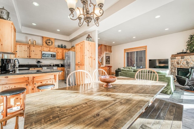 dining room with a chandelier, a stone fireplace, sink, and a tray ceiling