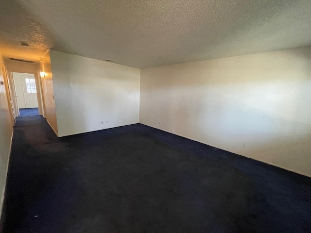 unfurnished room with a textured ceiling and dark carpet