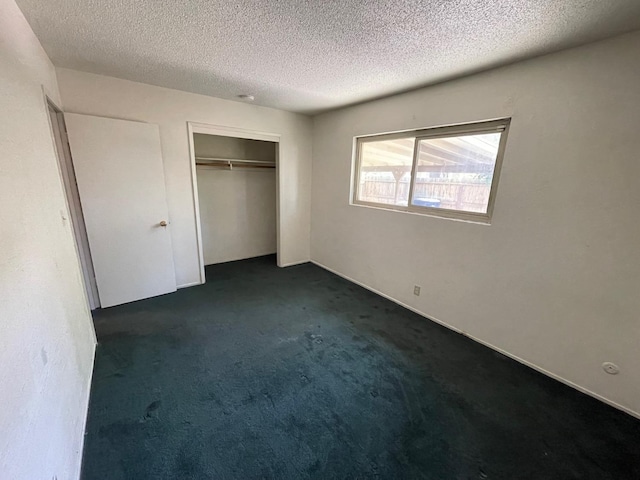 unfurnished bedroom with a textured ceiling, dark carpet, and a closet