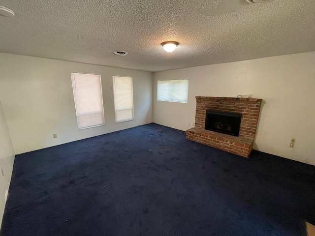 unfurnished living room featuring dark colored carpet, a textured ceiling, and a brick fireplace