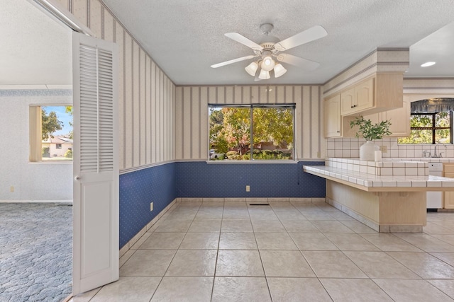 kitchen featuring ceiling fan, a textured ceiling, a kitchen bar, tile countertops, and kitchen peninsula