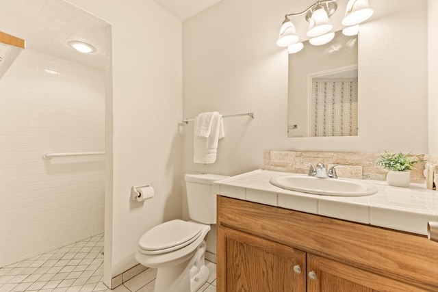 bathroom with tile patterned flooring, vanity, a tile shower, and toilet