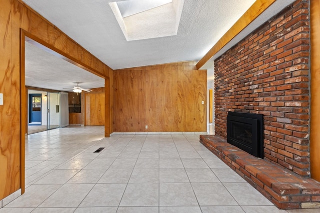 unfurnished living room featuring light tile patterned flooring, a textured ceiling, a fireplace, and wood walls