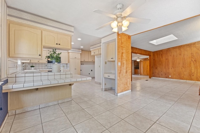 kitchen with a skylight, a kitchen breakfast bar, tile counters, kitchen peninsula, and wood walls