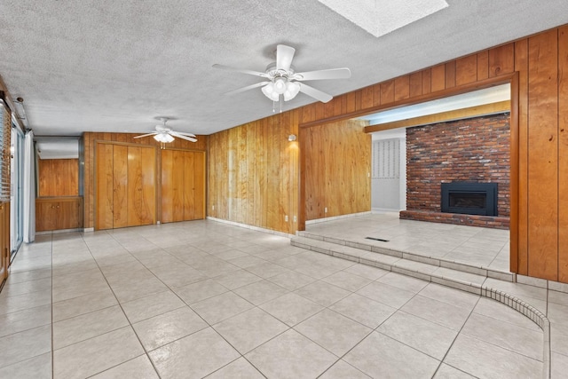 unfurnished living room featuring a fireplace, wood walls, a skylight, ceiling fan, and a textured ceiling