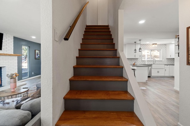 stairs featuring wood-type flooring and a brick fireplace