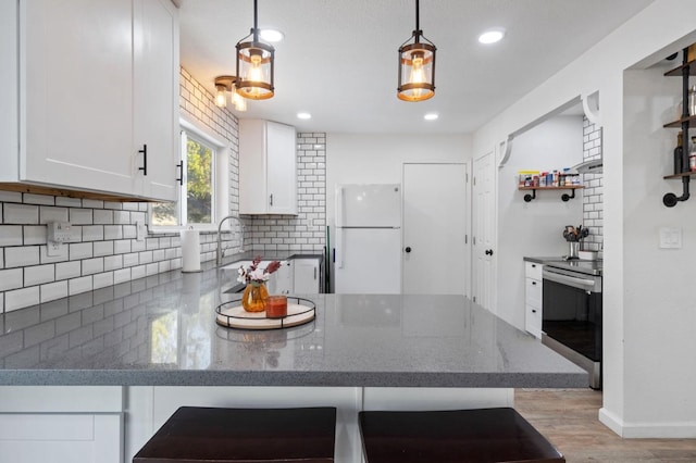 kitchen with white cabinetry, white refrigerator, stainless steel stove, light hardwood / wood-style floors, and decorative light fixtures