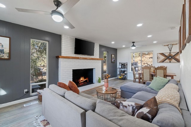 living room with light hardwood / wood-style flooring, a brick fireplace, and ceiling fan