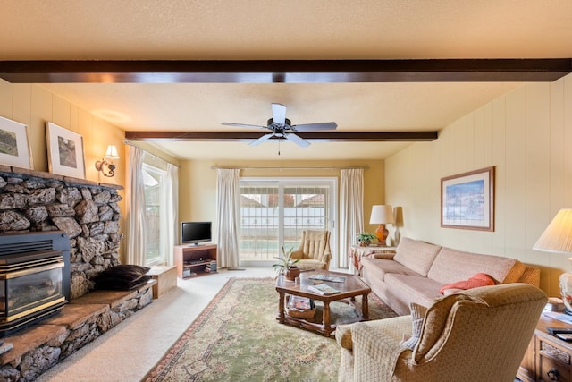 carpeted living room with beamed ceiling, a stone fireplace, ceiling fan, and wood walls