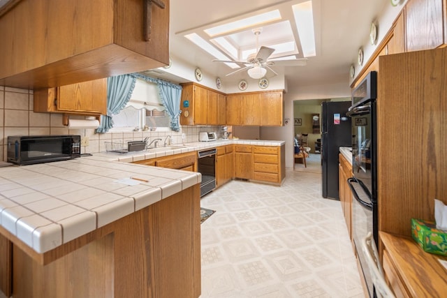 kitchen with tile countertops, black appliances, decorative backsplash, ceiling fan, and kitchen peninsula