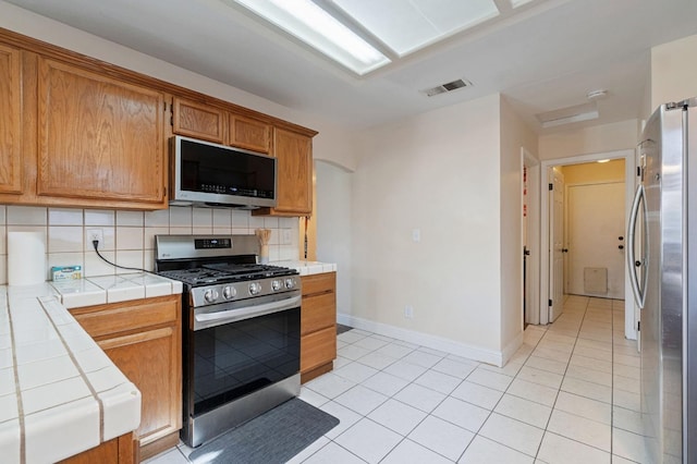 kitchen featuring backsplash, tile counters, light tile patterned floors, and stainless steel appliances