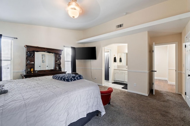 bedroom featuring light carpet, multiple windows, ensuite bathroom, and ceiling fan