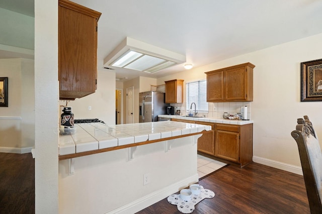 kitchen featuring a kitchen breakfast bar, dark hardwood / wood-style flooring, tile countertops, stainless steel fridge, and kitchen peninsula