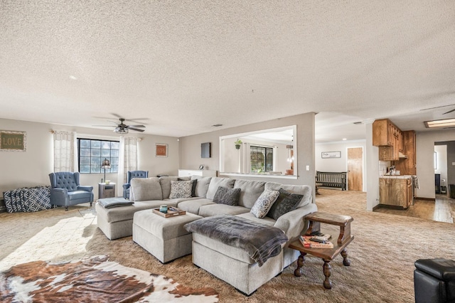 living room featuring ceiling fan, light colored carpet, and a textured ceiling