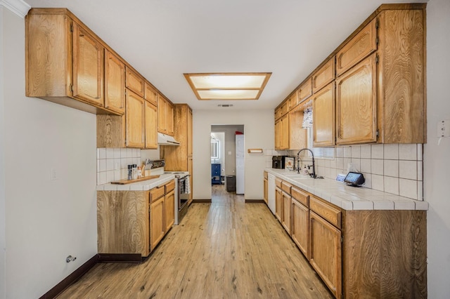 kitchen featuring sink, tile countertops, white dishwasher, stainless steel electric range, and light wood-type flooring