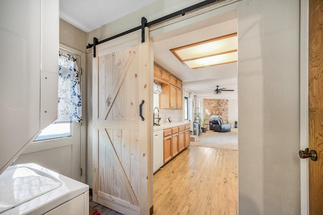 kitchen with ceiling fan, a barn door, light hardwood / wood-style flooring, backsplash, and white dishwasher