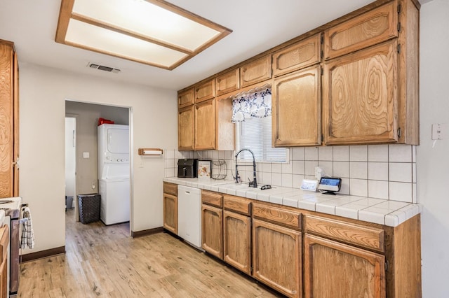 kitchen featuring stainless steel range, dishwasher, sink, light hardwood / wood-style floors, and stacked washer / drying machine