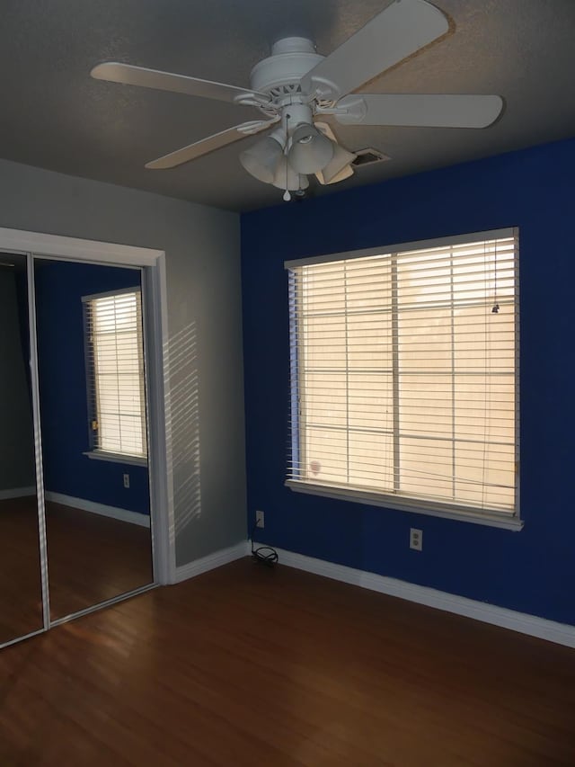 unfurnished bedroom with a closet, multiple windows, ceiling fan, and hardwood / wood-style floors