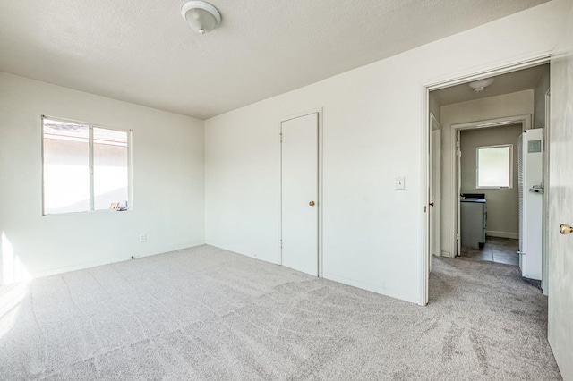 unfurnished bedroom featuring multiple windows, a closet, light colored carpet, and a textured ceiling