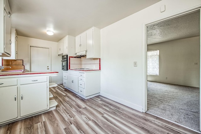 kitchen featuring tasteful backsplash, cooktop, white cabinets, light hardwood / wood-style floors, and oven