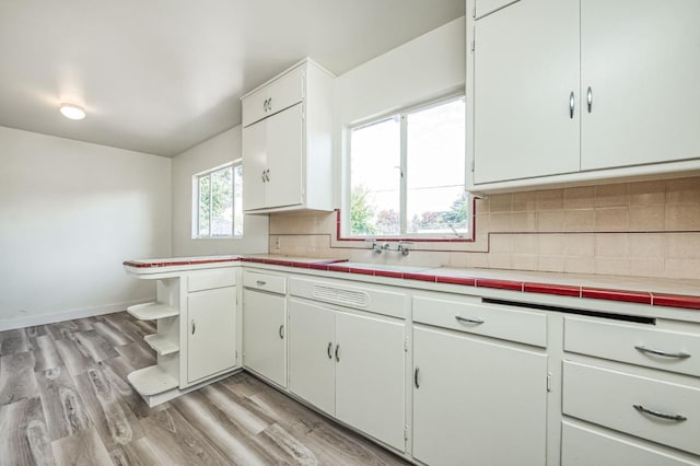 kitchen featuring light wood-type flooring, backsplash, sink, tile countertops, and white cabinetry