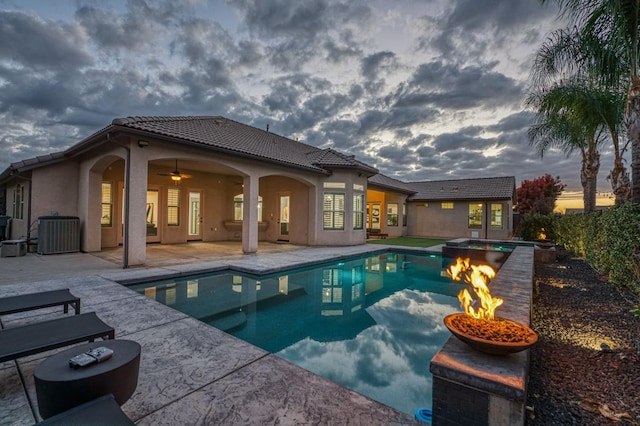 pool at dusk with ceiling fan, an in ground hot tub, and a patio