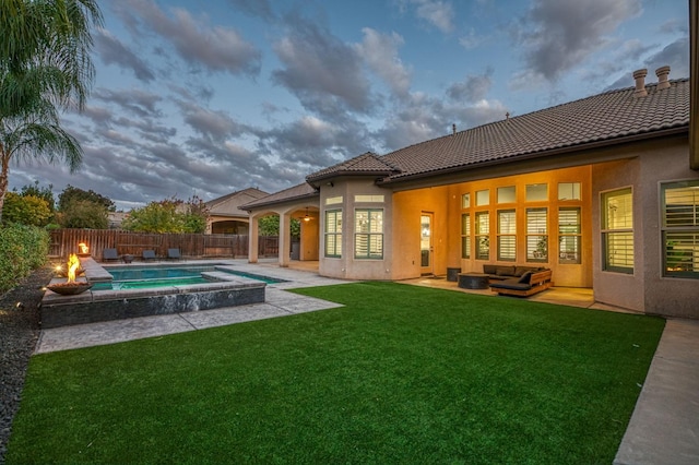 back house at dusk with a pool with hot tub, a patio area, a yard, and an outdoor living space with a fire pit