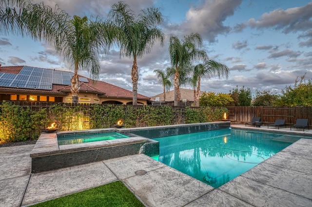 pool at dusk with an in ground hot tub and a patio