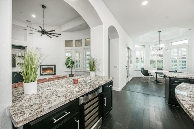 kitchen with hanging light fixtures, wine cooler, light stone countertops, a kitchen island, and dark hardwood / wood-style flooring