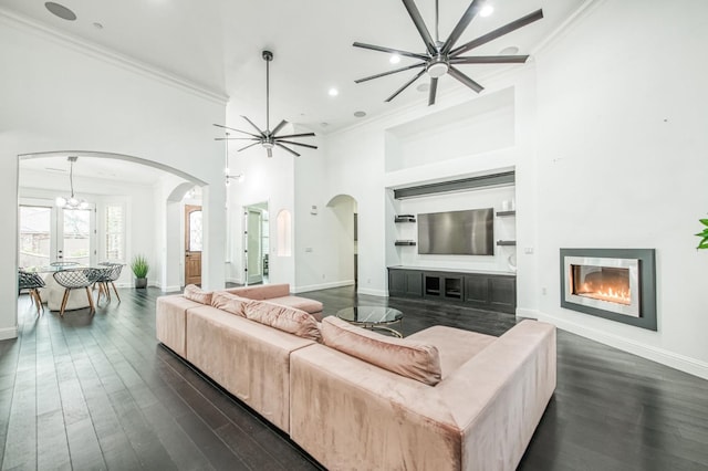 living room featuring ceiling fan with notable chandelier, a high ceiling, dark hardwood / wood-style flooring, and crown molding