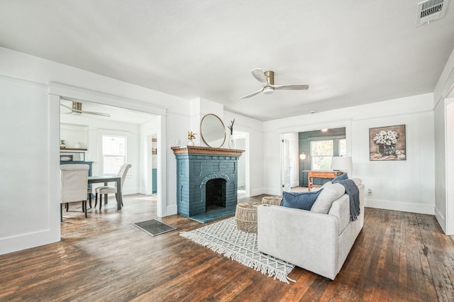 living room with ceiling fan, dark hardwood / wood-style flooring, a wealth of natural light, and a brick fireplace