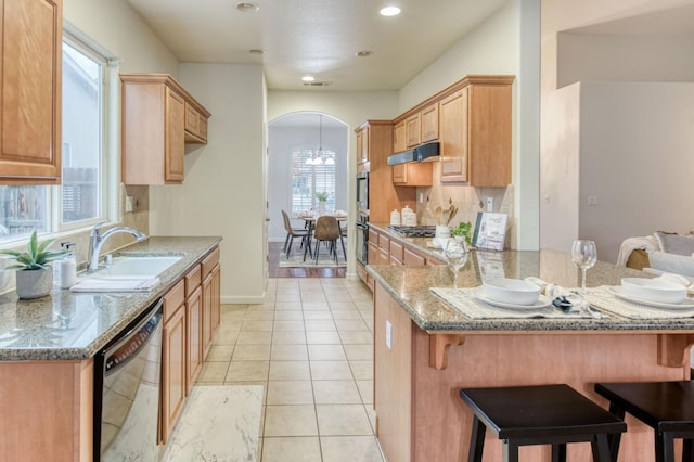 kitchen with stone counters, a breakfast bar, range hood, black dishwasher, and sink