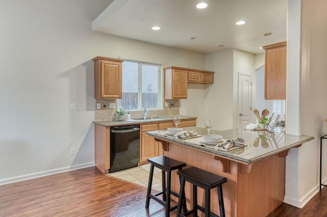 kitchen with light hardwood / wood-style flooring, dishwasher, a kitchen breakfast bar, light stone counters, and kitchen peninsula