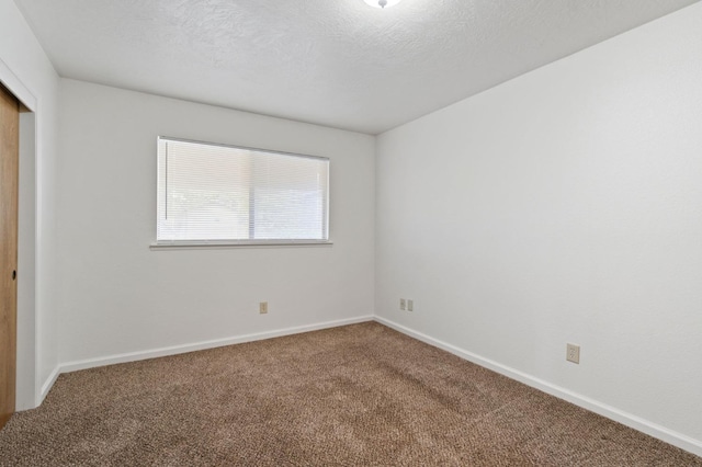 unfurnished room with carpet, baseboards, and a textured ceiling