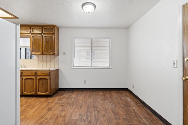 kitchen with decorative backsplash, dark wood-style flooring, baseboards, and brown cabinetry