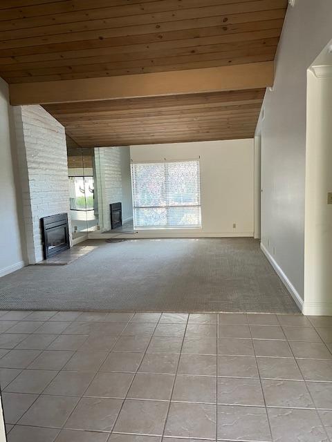 unfurnished living room featuring a fireplace, lofted ceiling with beams, light colored carpet, and wood ceiling