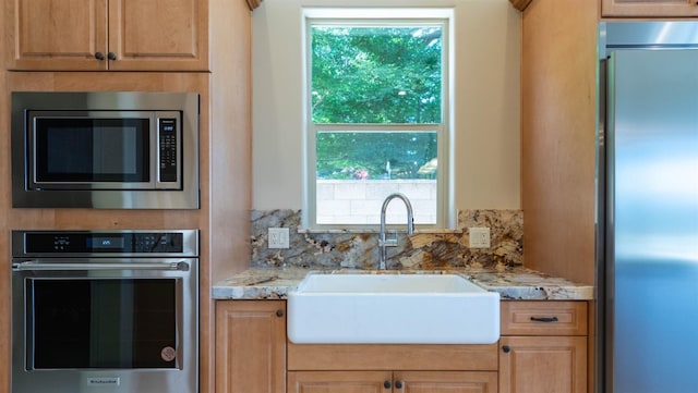 kitchen with a sink, decorative backsplash, built in appliances, and light stone countertops