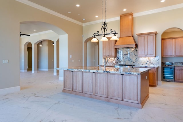 kitchen with light stone countertops, custom exhaust hood, beverage cooler, decorative light fixtures, and a center island with sink