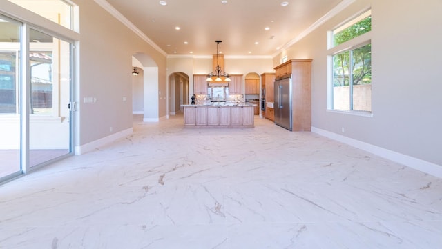 kitchen featuring high end refrigerator, light stone counters, ornamental molding, decorative light fixtures, and a center island with sink