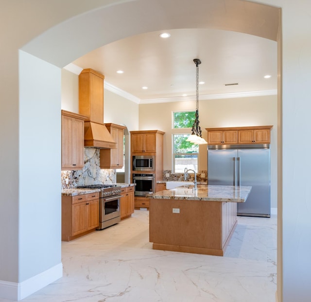 kitchen featuring light stone counters, a kitchen island with sink, sink, pendant lighting, and built in appliances