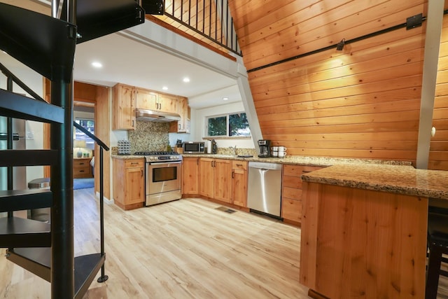 kitchen with tasteful backsplash, light stone counters, kitchen peninsula, appliances with stainless steel finishes, and light wood-type flooring