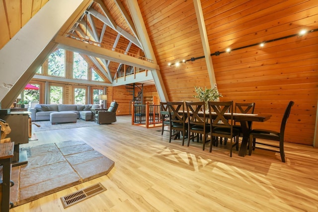 dining room featuring beam ceiling, high vaulted ceiling, wooden walls, wood ceiling, and light wood-type flooring