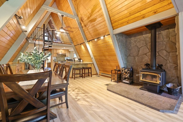 dining area with beamed ceiling, light hardwood / wood-style flooring, a wood stove, and wood ceiling